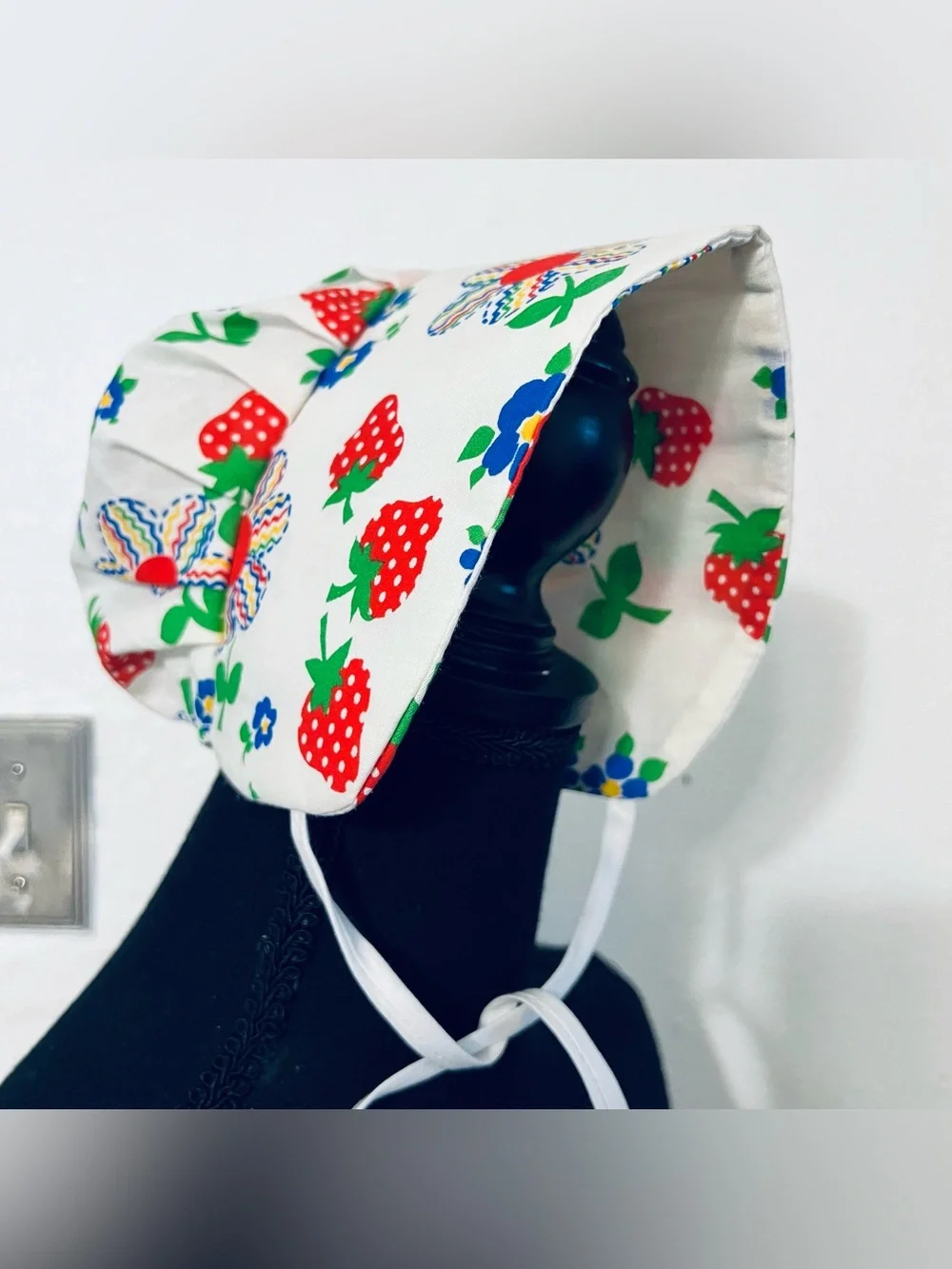 Charming vintage-style baby sunbonnet features a playful white fabric patterned